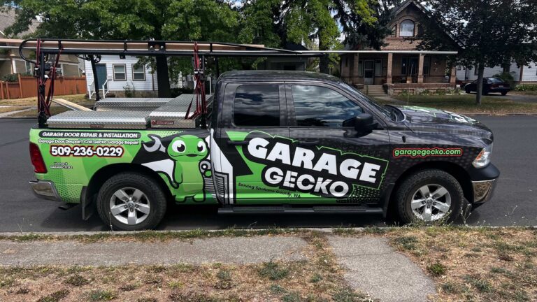Fully wrapped Garage Gecko Repair truck parked outside of a house in Spokane with a roof rack and toolboxes in the bed of the truck.